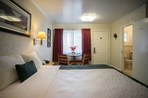 Une chambre d’hôtel comprenant un lit, un bureau avec une chaise, une fenêtre avec des rideaux et une porte donnant sur une salle de bain.