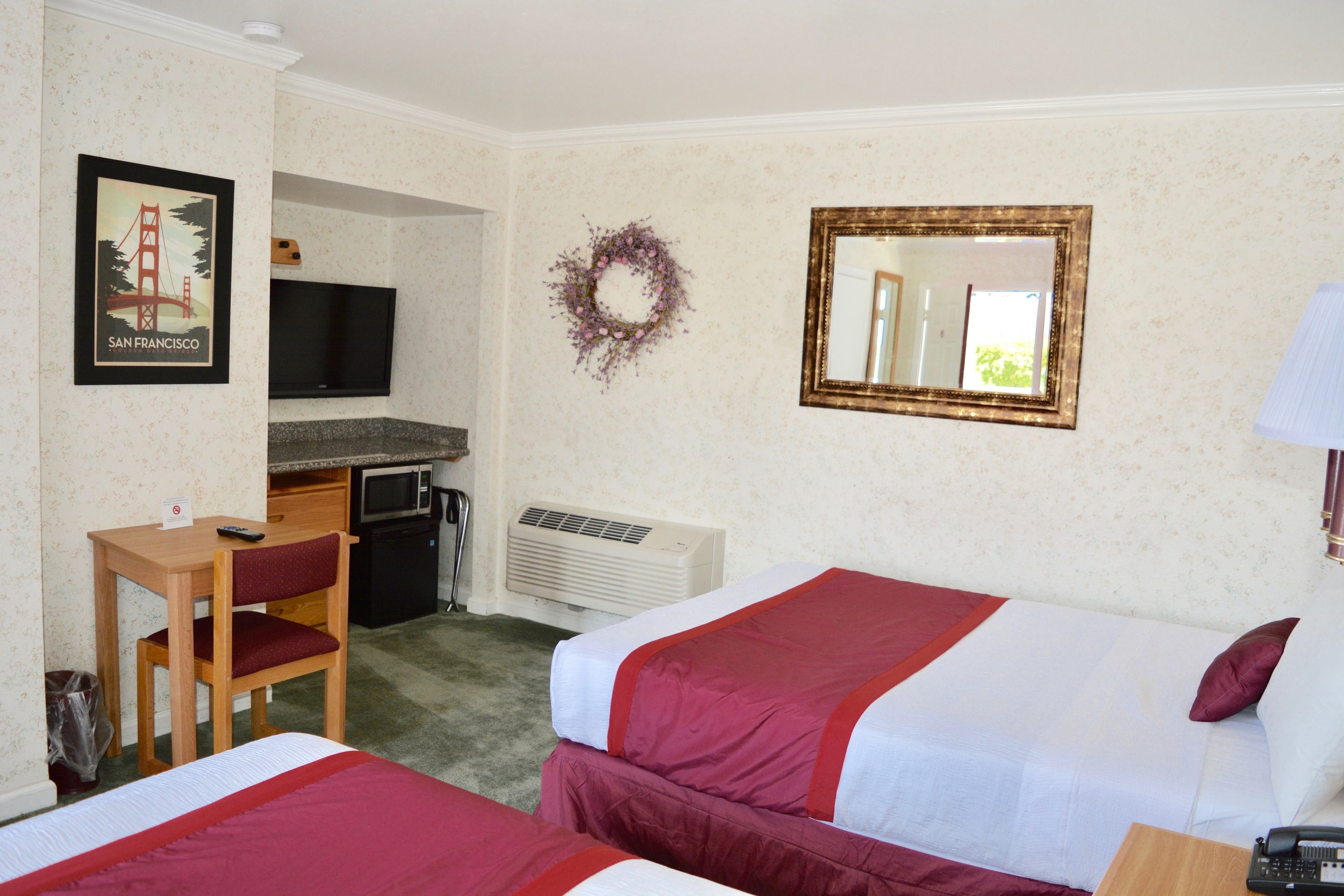 Habitación de hotel con dos camas, un escritorio con silla, un televisor, un espejo y un adorno en la pared.