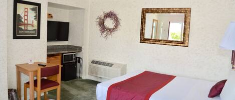 Habitación de hotel con dos camas, un escritorio con silla, un televisor, un espejo y un adorno en la pared.