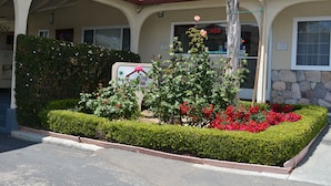 A hotel entrance with a landscaped garden, a signboard, and a tiled roof. - Travelers Inn (South San Francisco)