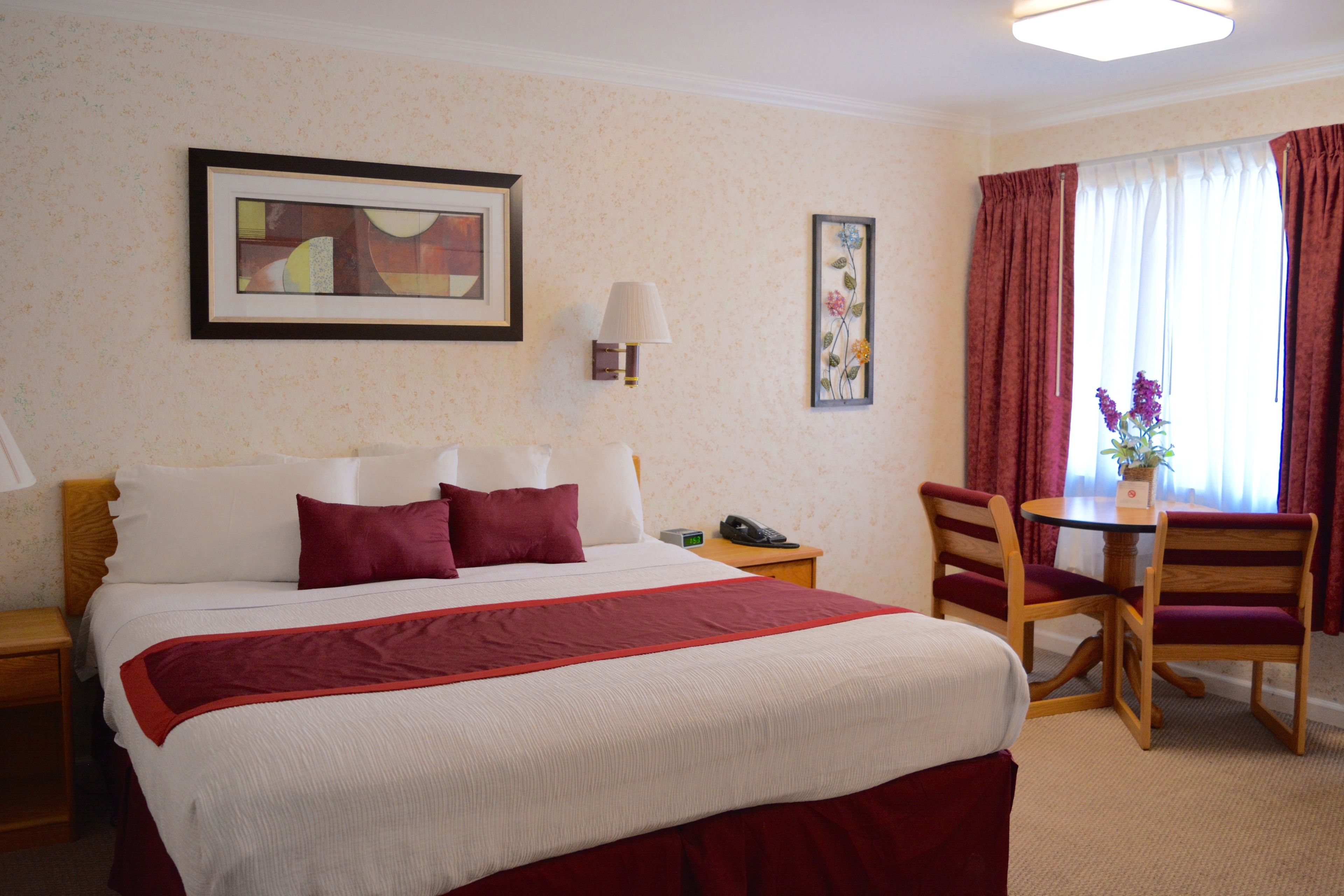 Une chambre d’hôtel comprenant un lit, une table de chevet, une lampe, un tableau encadré et un coin repas avec des chaises et une table.