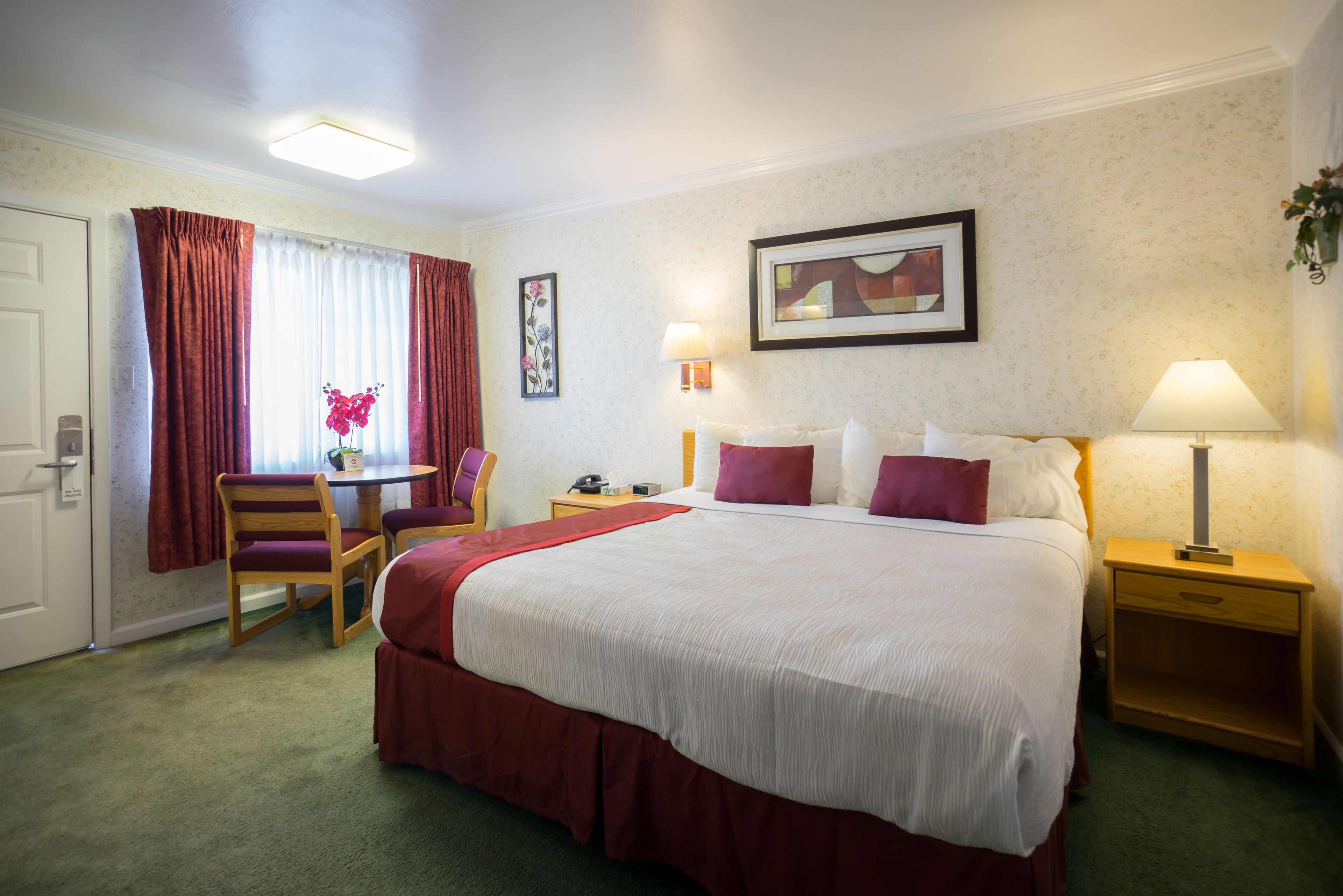 A hotel room with a large bed, two bedside tables, a desk with a chair, and a window with curtains.