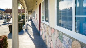 A covered walkway with stone walls and large windows. - Travelers Inn (South San Francisco)