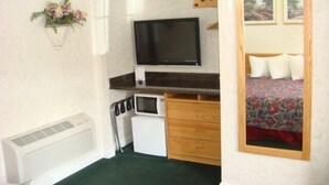 A compact room with a bed, a television, a small white refrigerator, and a heater. - Travelers Inn (South San Francisco)