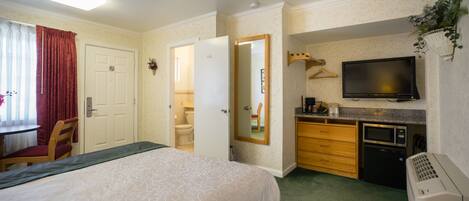 A hotel room with a bed, a desk, a chair, a television, a microwave, and a small kitchenette.