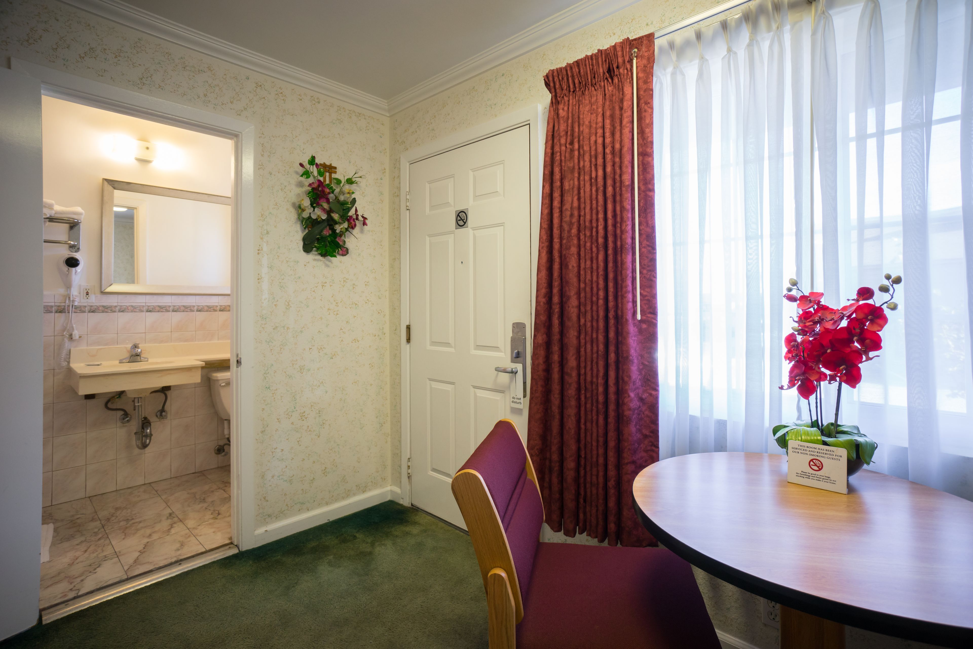 A hotel room with a bathroom, a dining area with a table and chair, and a window with curtains.