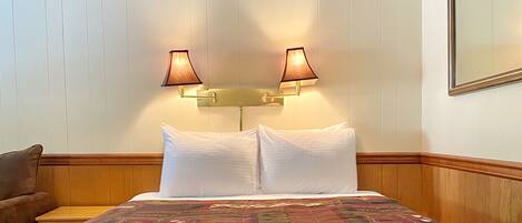A hotel room with a bed, two wall-mounted lamps, and a wooden headboard.