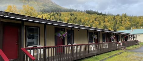 A motel with a covered porch, multiple rooms, and a mountain backdrop.