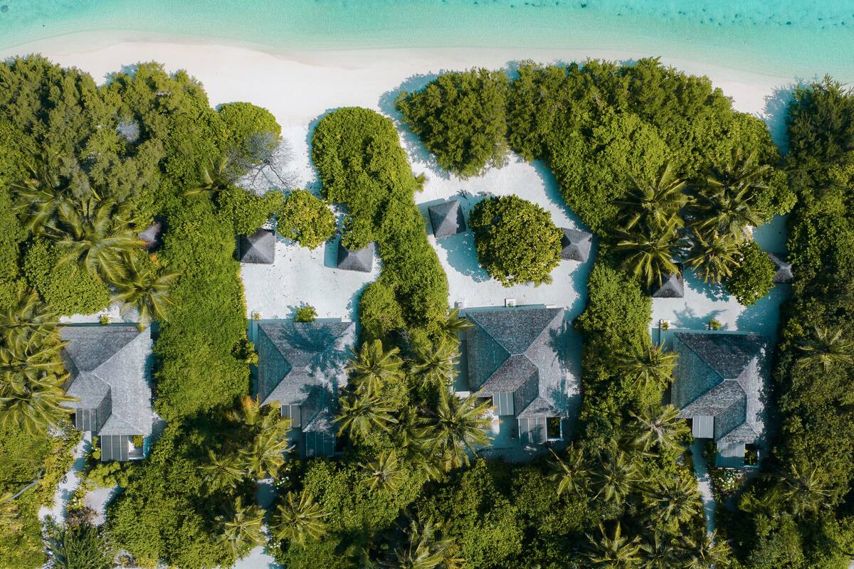 Vista aérea de un complejo turístico con varias edificaciones rodeadas de exuberante vegetación tropical y aguas turquesa cristalinas.