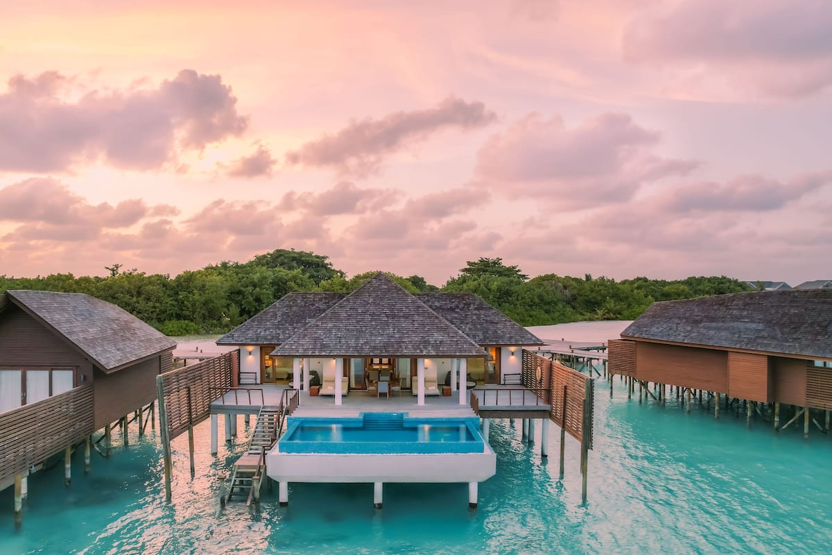 Bungalows sobre el agua con piscina, pasarelas de madera y vista al atardecer.