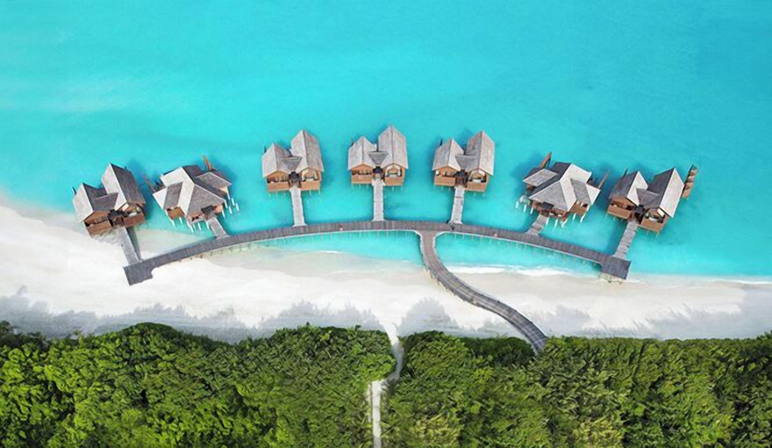 Vista aérea de un resort con una serie de bungalows sobre el agua conectados por un puente.