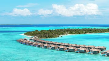 Un resort sobre el agua con bungalows de techo de paja conectados por pasarelas sobre aguas turquesas cristalinas.