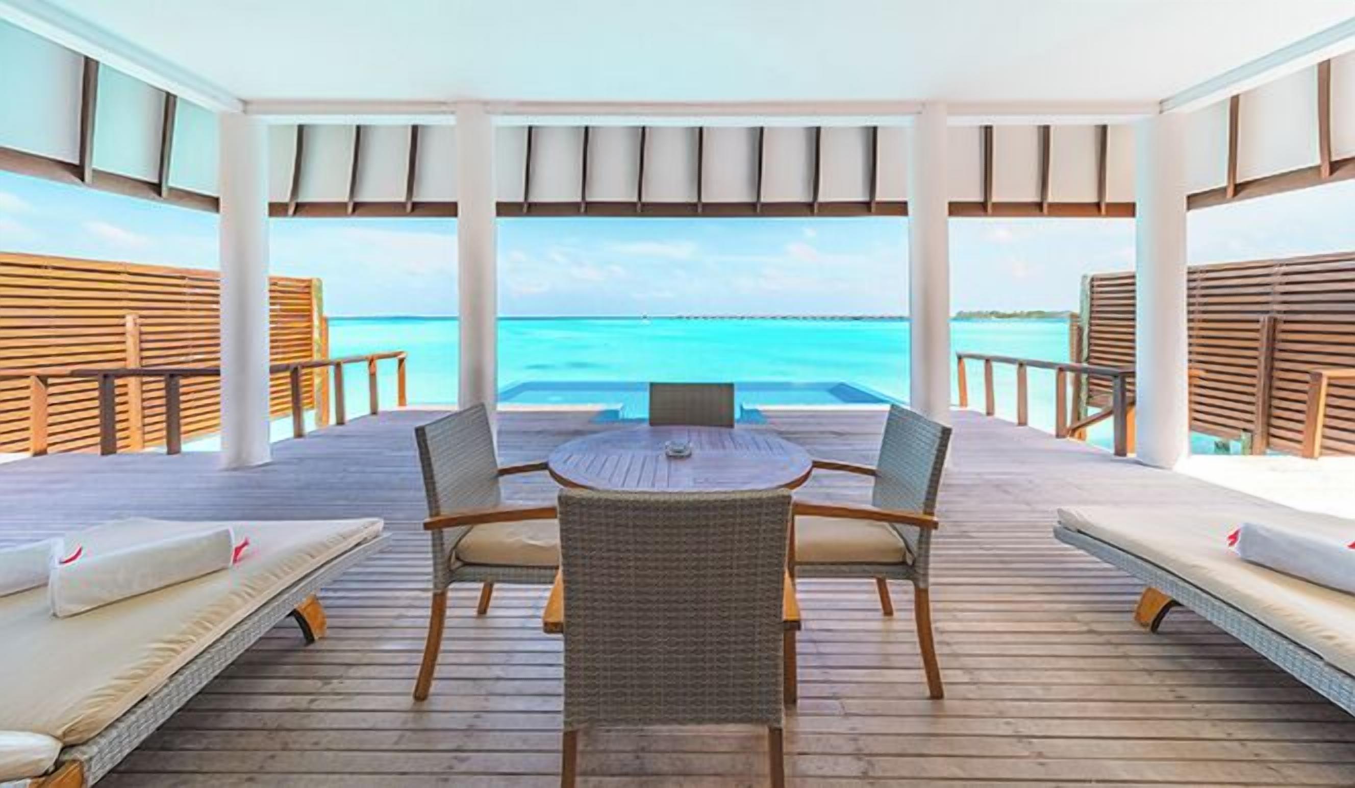 A covered outdoor seating area with a table and chairs, overlooking a turquoise sea.