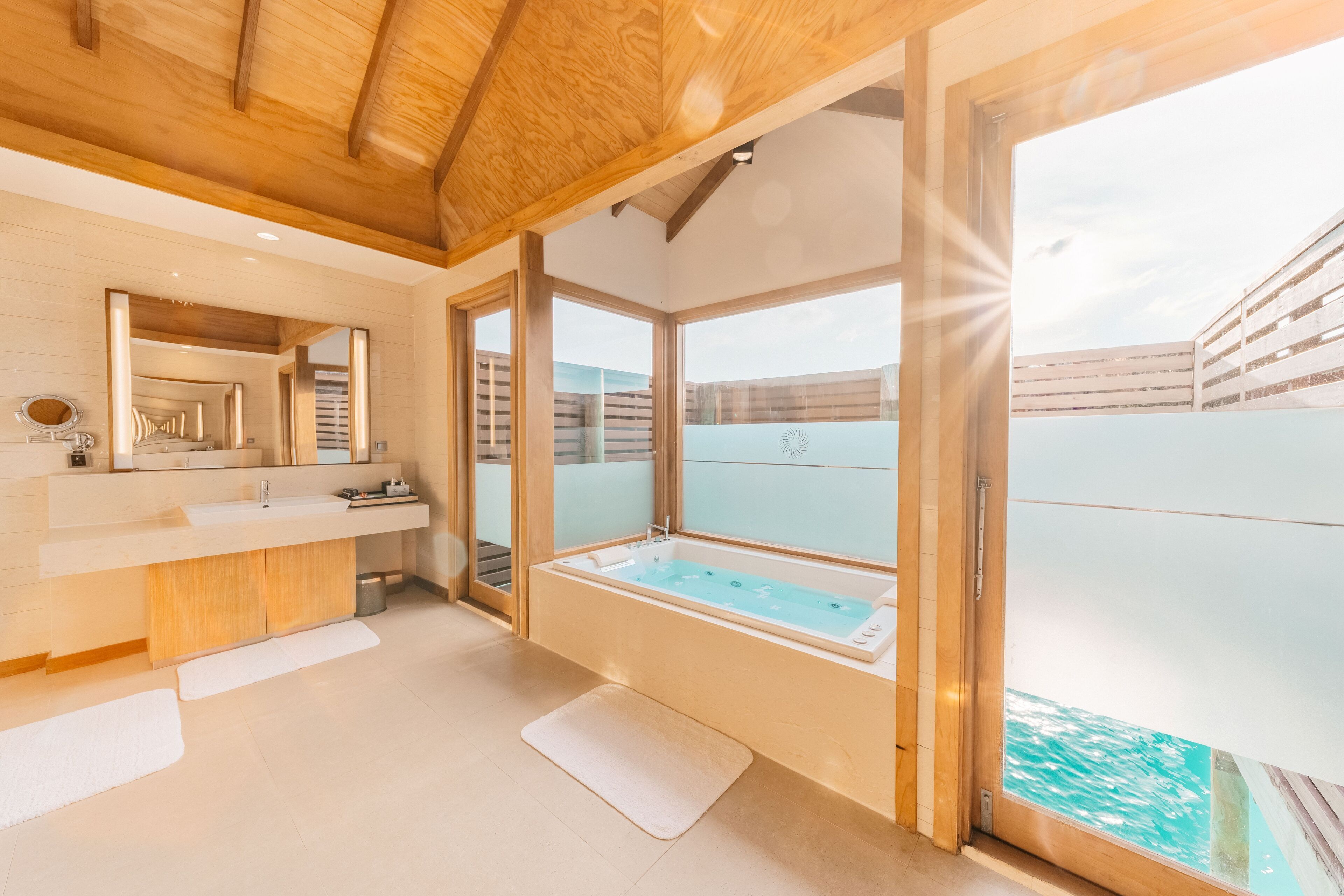 Uma casa de banho moderna com uma banheira grande, uma toucador com espelho e vista para uma piscina através de amplas portas de vidro.