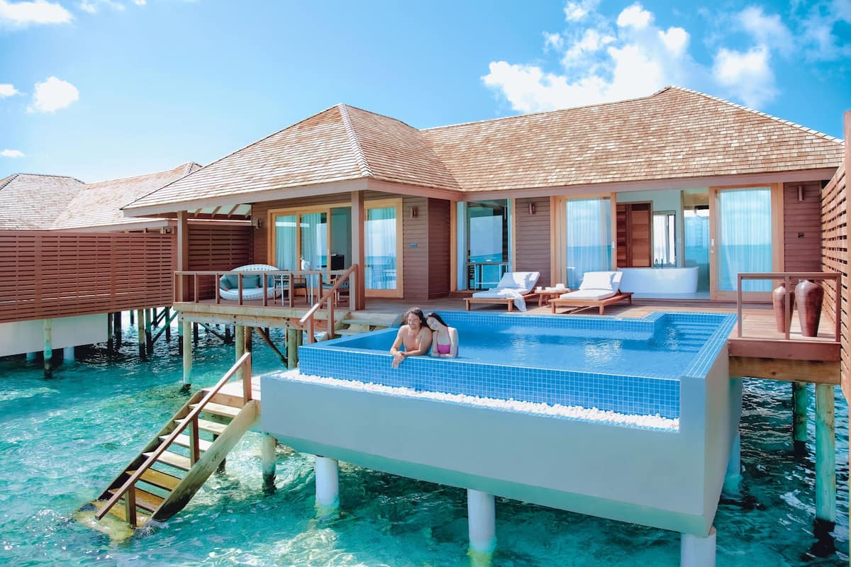 Una lujosa villa sobre el agua con piscina privada, terraza de madera y puertas de cristal que dan al interior.