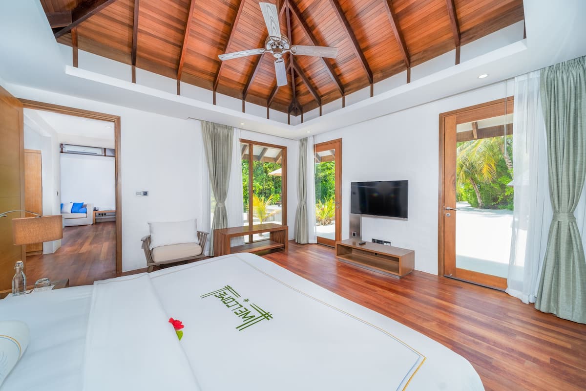 Un dormitorio amplio con una cama grande, ventilador de techo, televisor y vistas a zonas verdes.