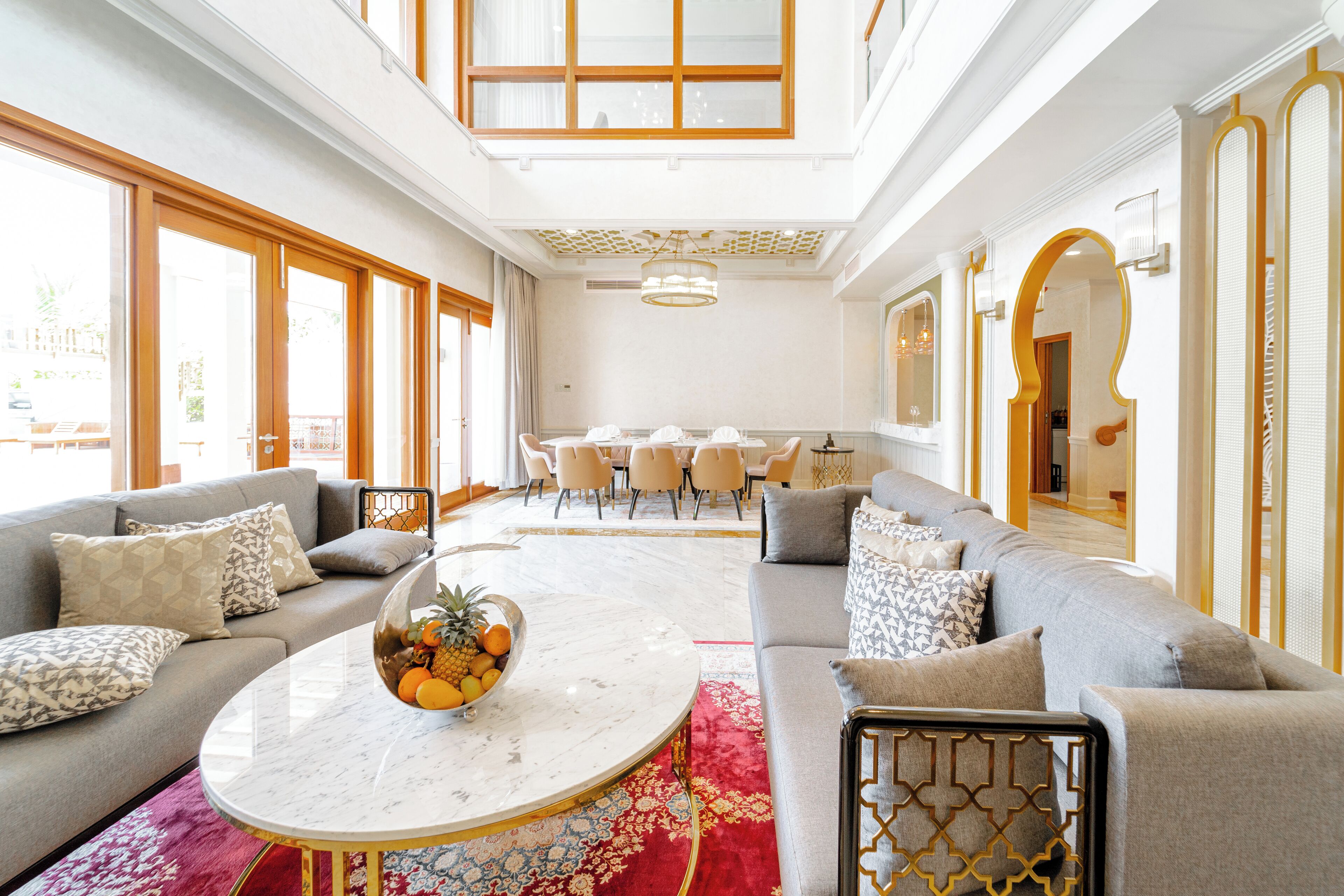 A spacious living area with a marble coffee table, grey sofas, and a dining area in the background.