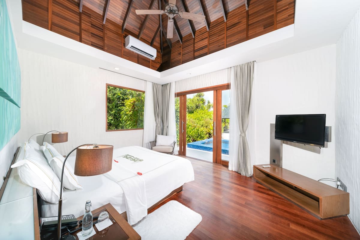 Habitación de hotel moderna con techo de madera, una cama grande, televisión y vista a una piscina.