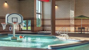 An indoor swimming pool with a basketball hoop, a hot tub, and a table with an umbrella.