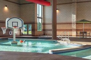 An indoor swimming pool with a basketball hoop, a hot tub, and a table with an umbrella. - Holiday Inn Stevens Point - Convention Ctr by IHG (Stevens Point)