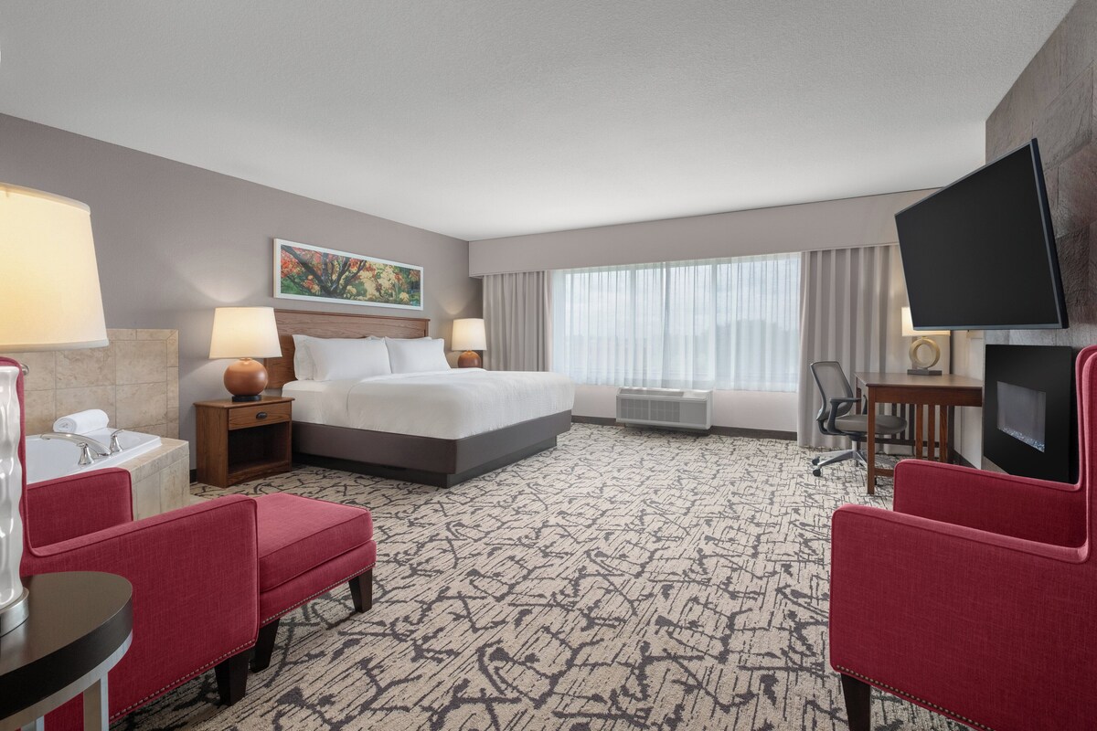 A hotel room with a bed, a desk, a chair, a TV, and a window with curtains.
