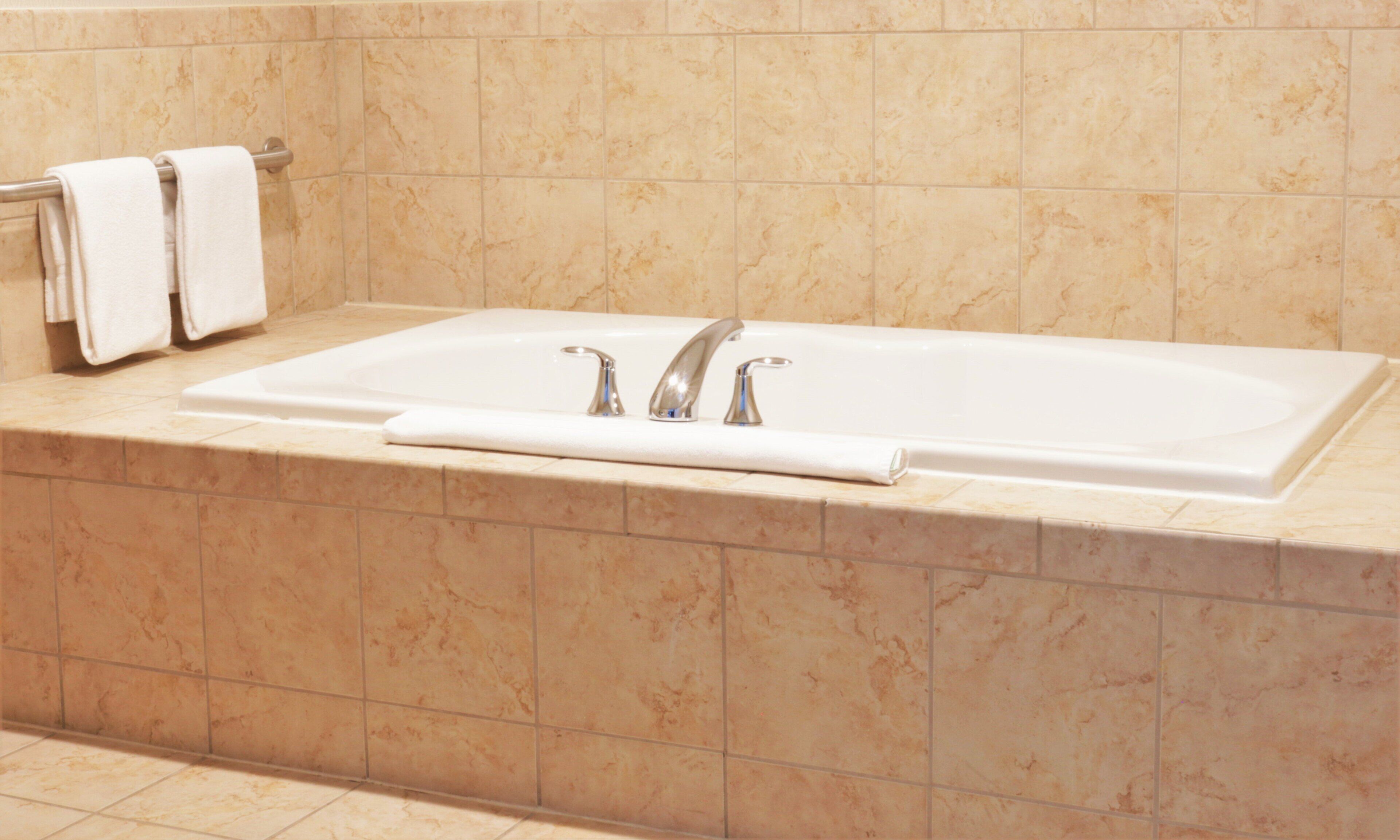 Un baño con una bañera grande, dos llaves y un perchero con dos toallas.