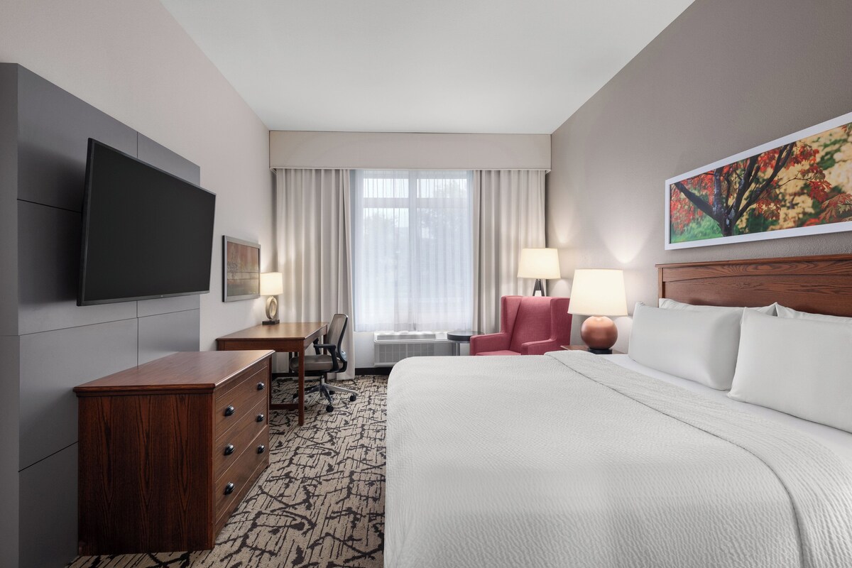 A hotel room with a bed, a desk, a chair, a television, and a painting on the wall.
