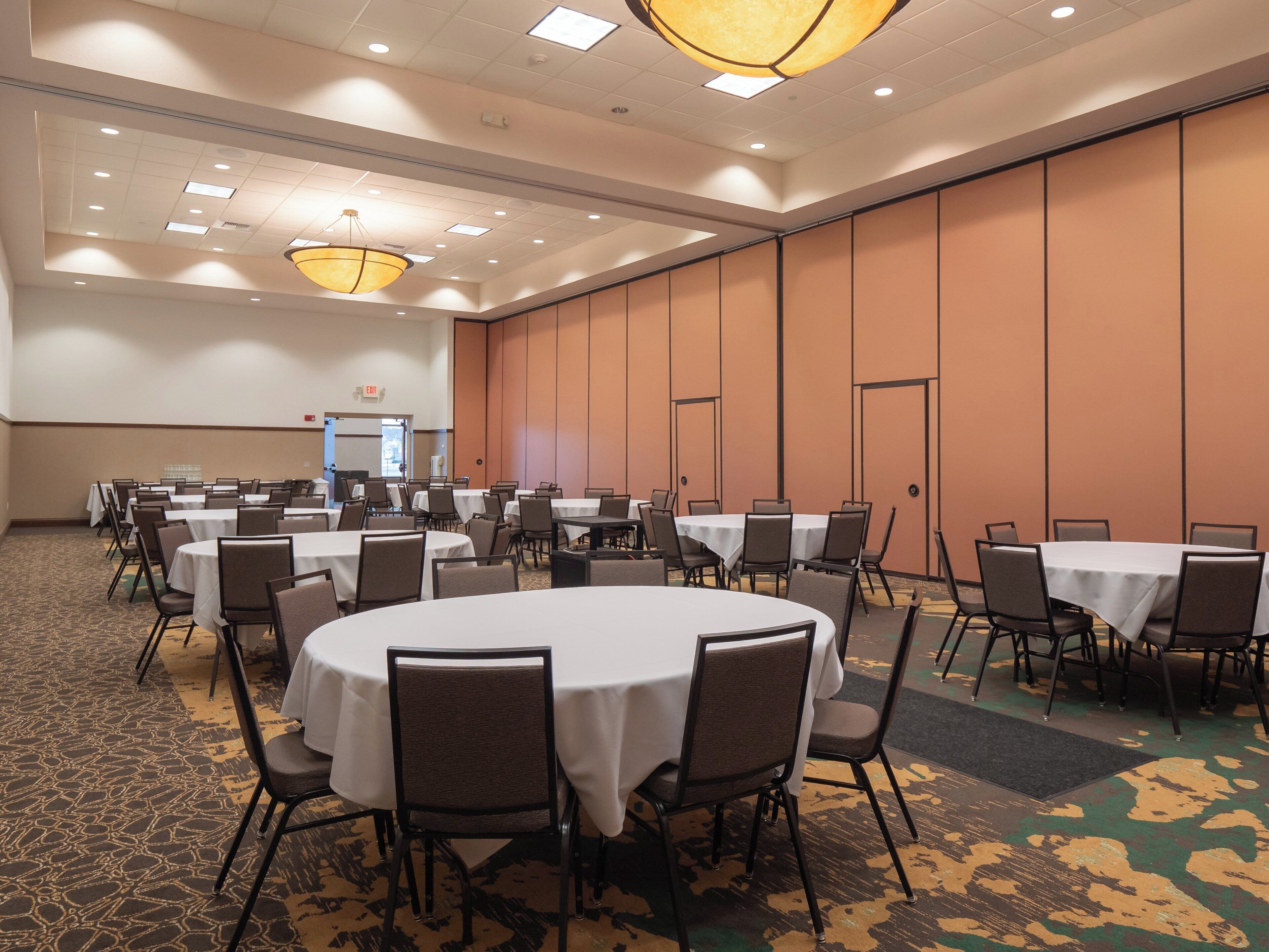 A conference room with multiple tables and chairs, a patterned carpet, and a plain wall with a door in the background.