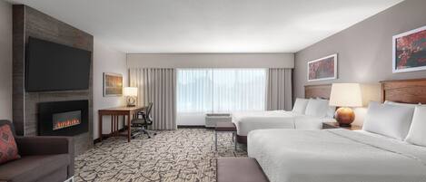 A hotel room with a fireplace, a TV, a desk, a bed, and a window with curtains.