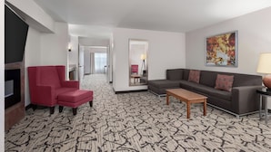 Habitació d'hotel amb un disseny de mosaic al terra, una poltrona vermella, un sofà gris, una taula de centre de fusta i un quadre a la paret.