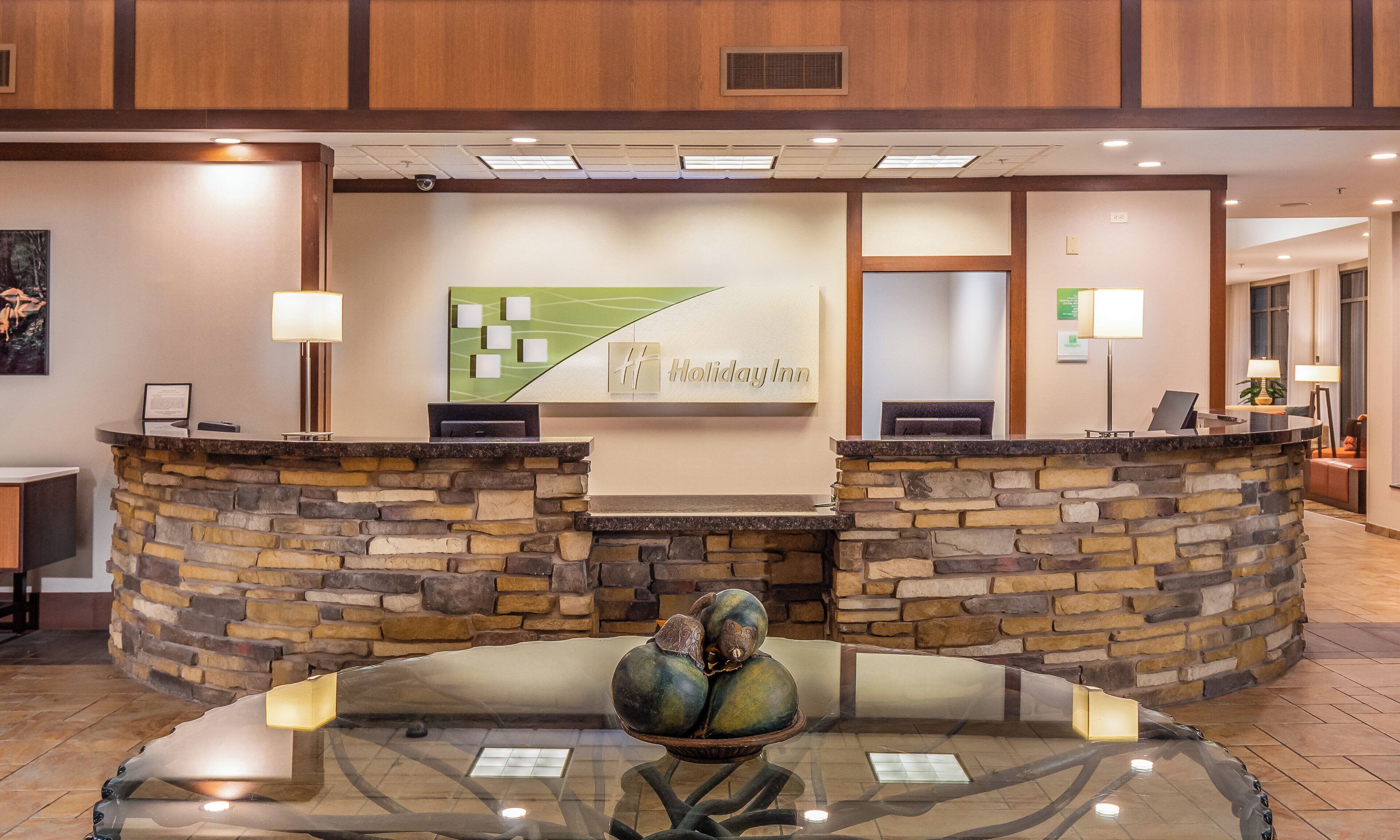 A reception area with a stone counter, a glass table with a decorative centerpiece, and a wall-mounted sign for Holiday Inn.