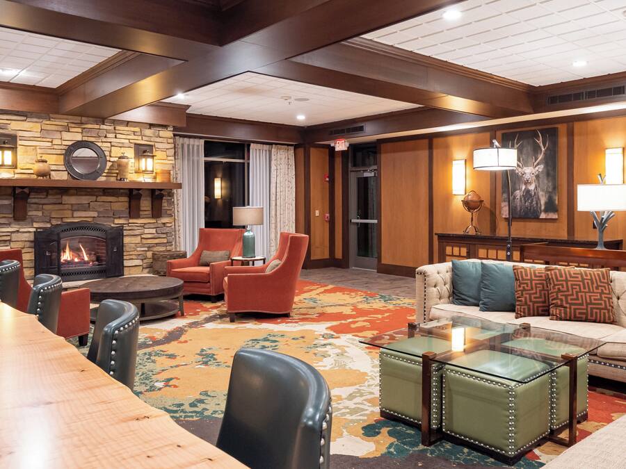 A hotel lobby with a fireplace, leather chairs, a sofa, a glass coffee table, and a patterned rug.