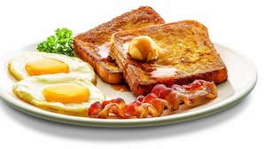 A plate with two fried eggs, toast, bacon, and a butter pat.