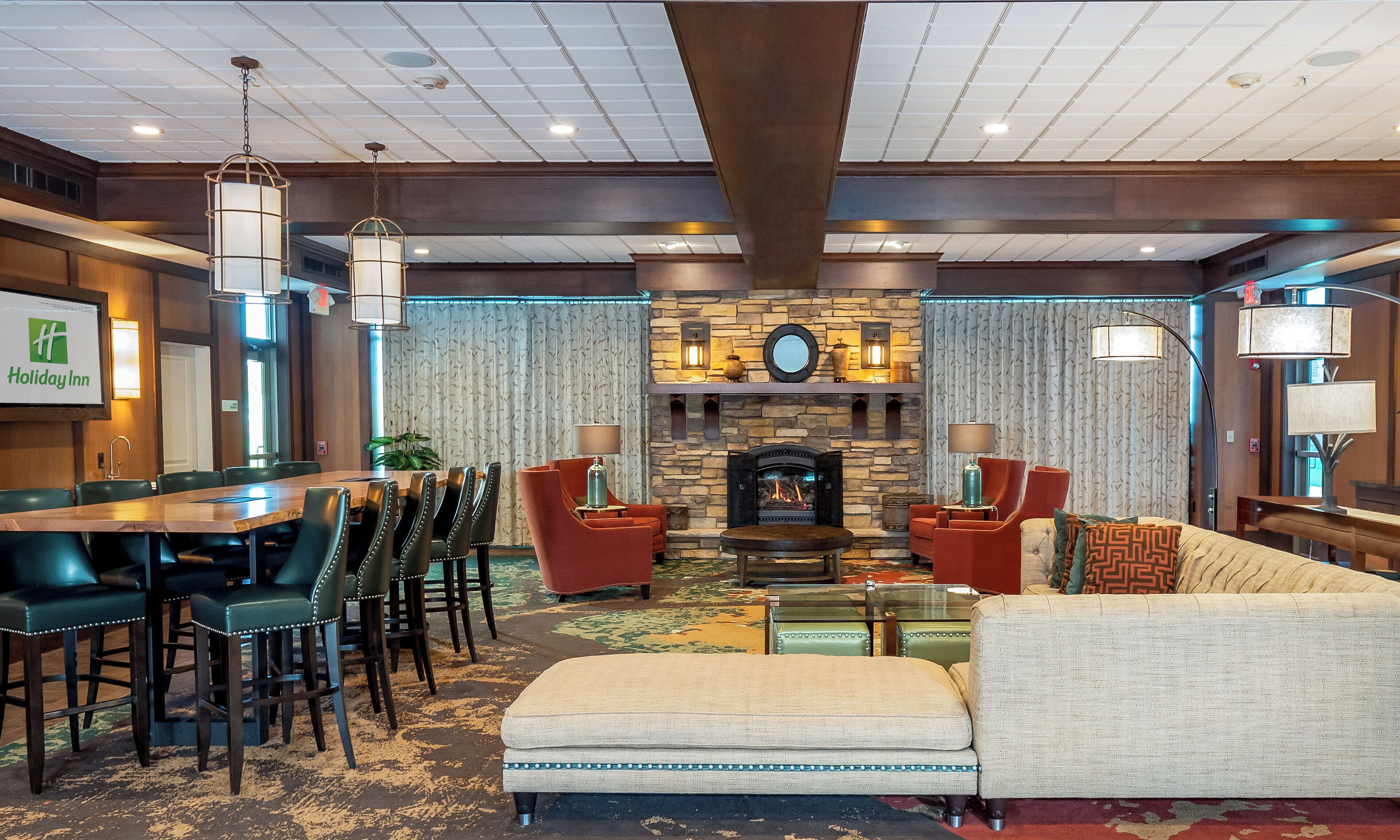 A Holiday Inn lobby with a stone fireplace, leather chairs, a sofa, and a dining area.