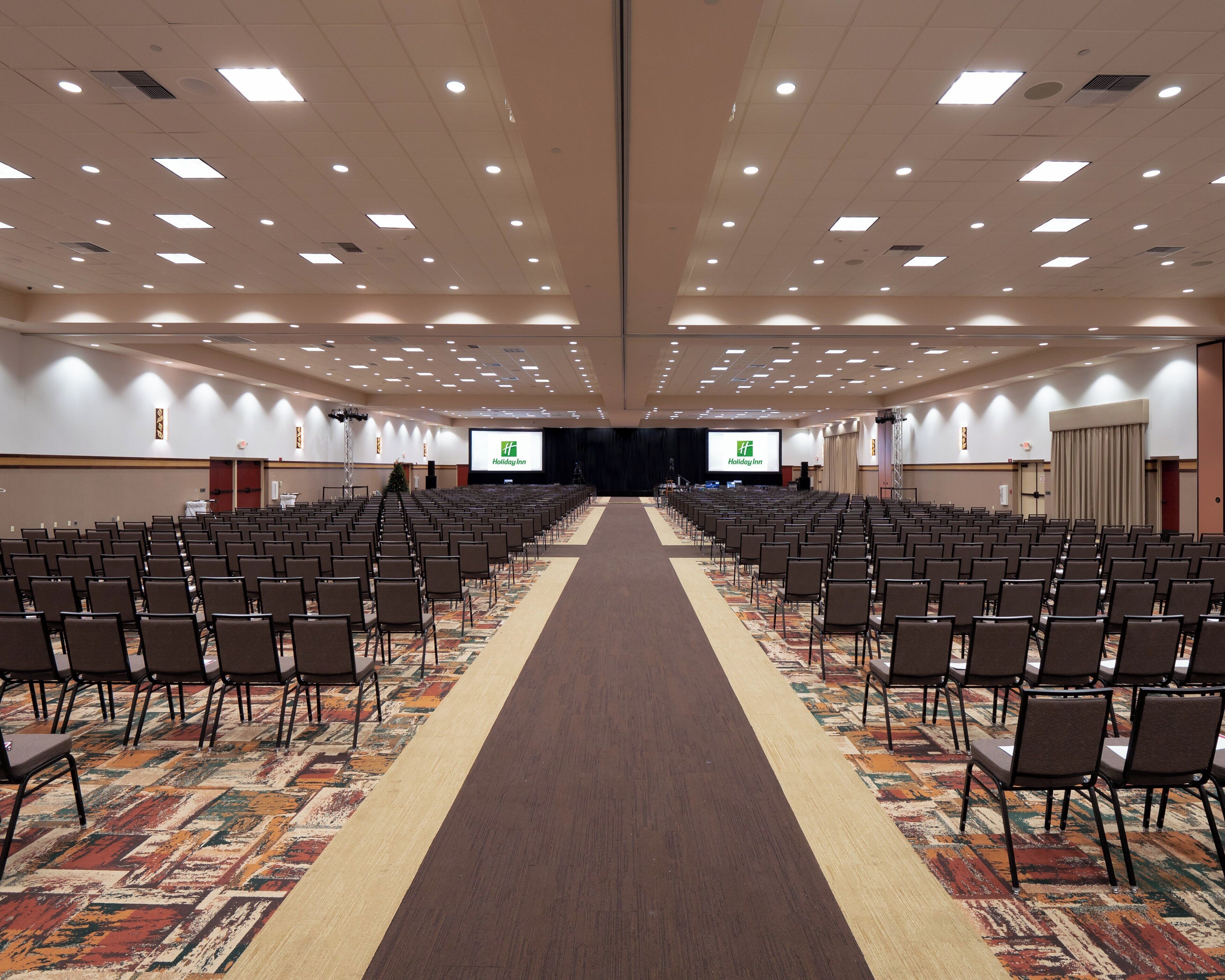 A large conference room with rows of chairs, a carpeted floor, and a stage at the front.
