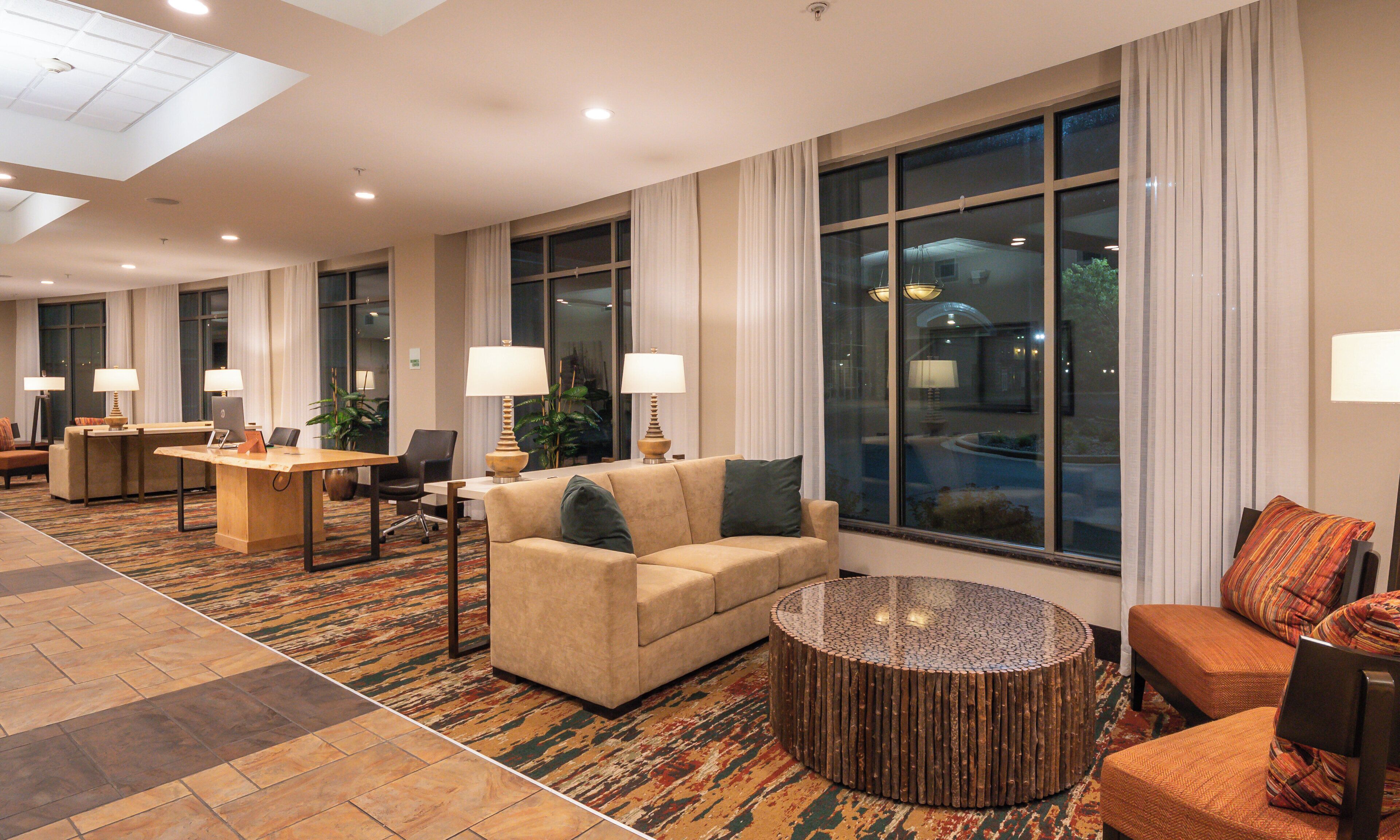 A hotel lobby with a reception desk, seating area, and large windows.