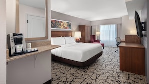 A hotel room with a large bed, a desk with a coffee maker, a TV, and a painting on the wall.