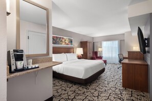 A hotel room with a large bed, a desk with a coffee maker, a TV, and a painting on the wall. - Holiday Inn Stevens Point - Convention Ctr by IHG (Stevens Point)