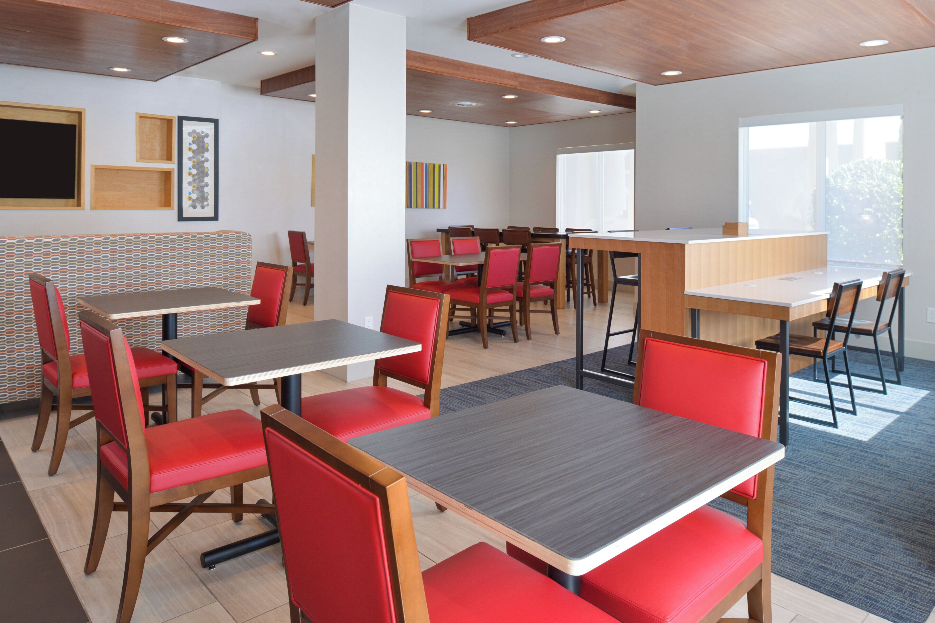 A modern dining area with multiple tables and chairs, wooden accents, and artwork on the walls.