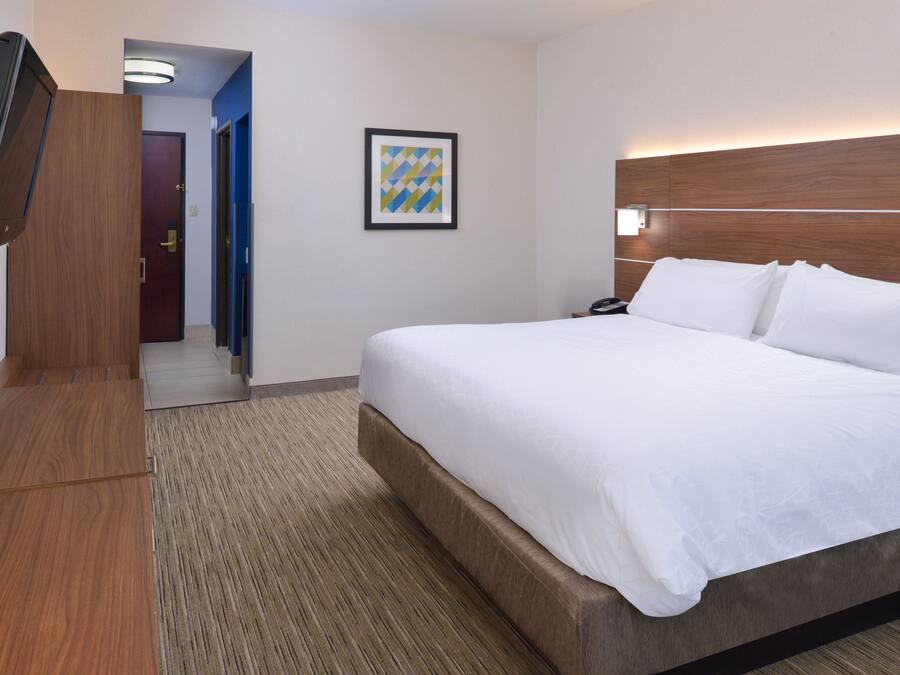 Une chambre d’hôtel avec un grand lit, une tête de lit en bois, un téléviseur à écran plat fixé au mur et une œuvre d’art encadrée accrochée au mur.