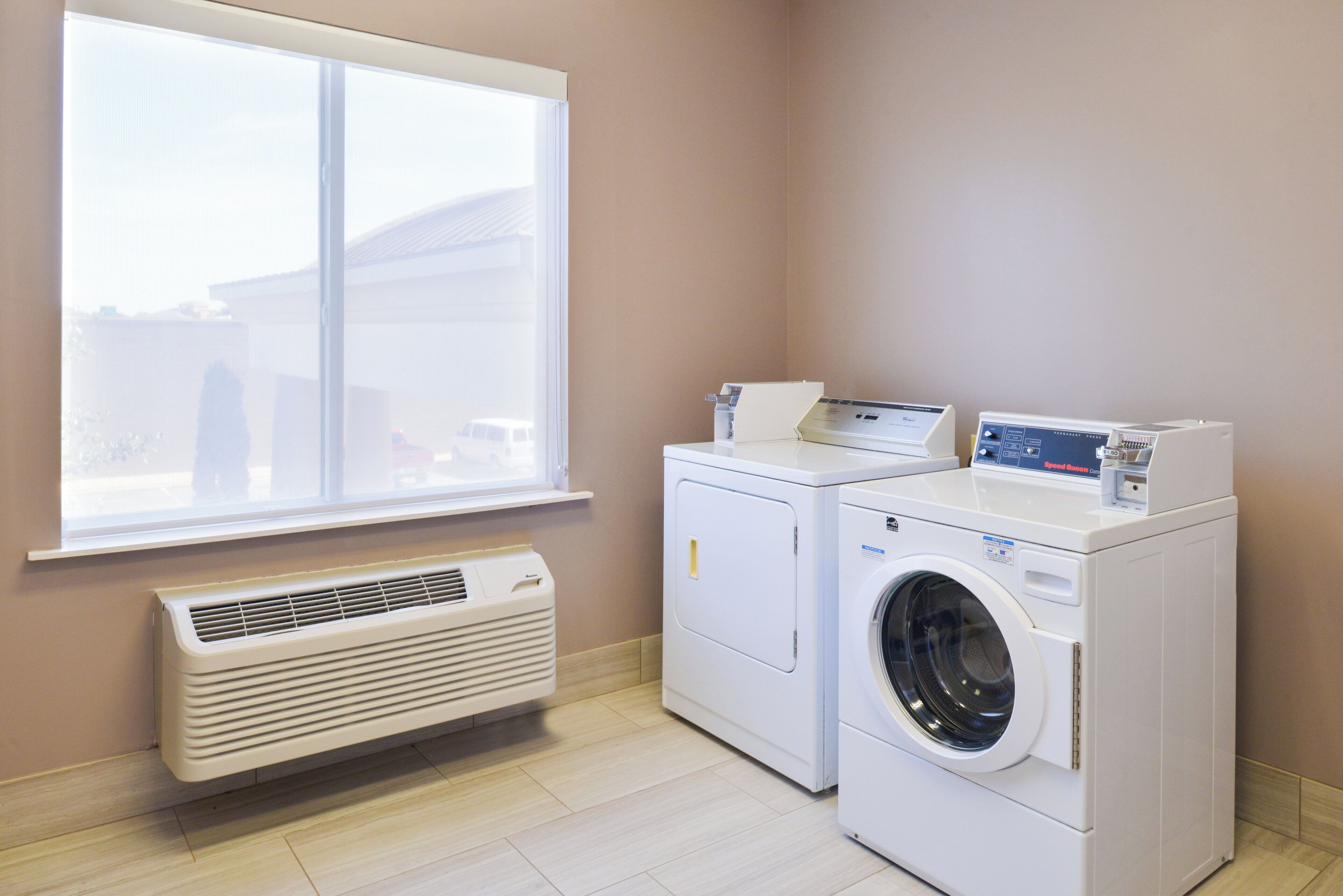 A laundry room with two stacked washers and dryers, a window, and a wall-mounted air conditioner.