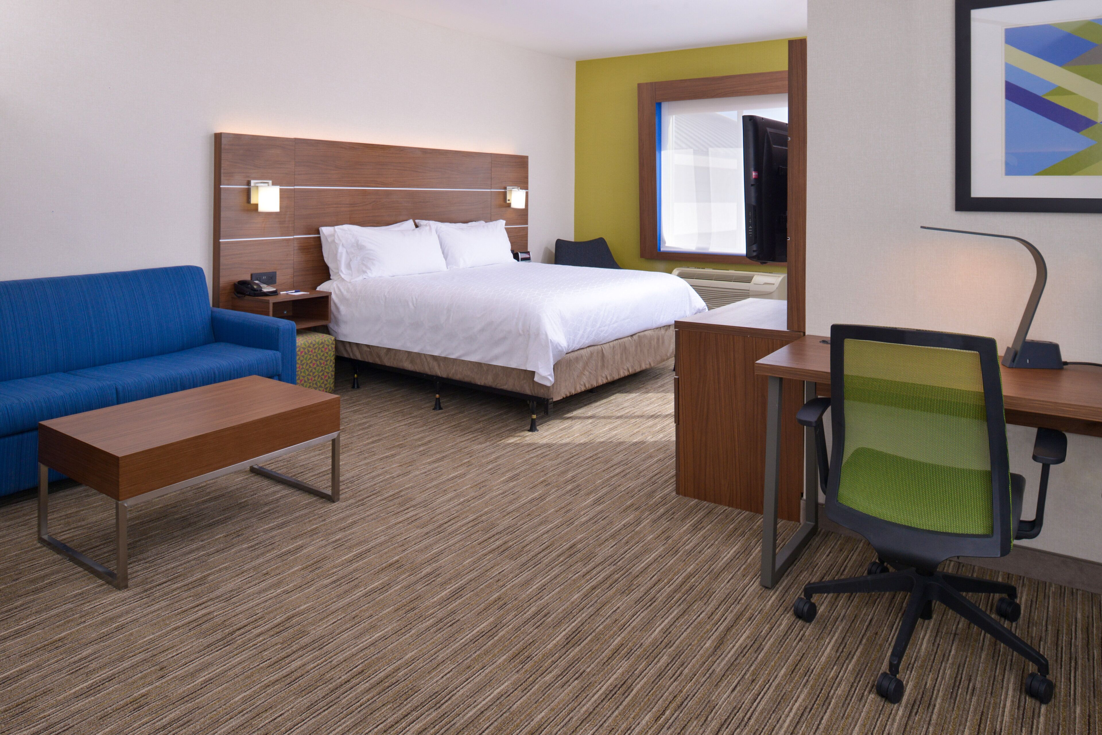 A hotel room with a bed, a desk, a chair, a sofa, and a TV.