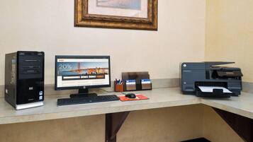 A hotel desk with a desktop computer, a monitor displaying a travel rewards program, and a printer.