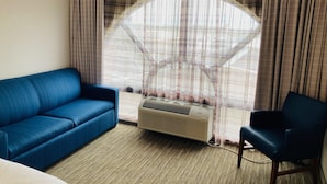 A room with a blue sofa, a chair, a large window with curtains, and an air conditioning unit. - Holiday Inn Express & Suites Abilene by IHG (Abilene)