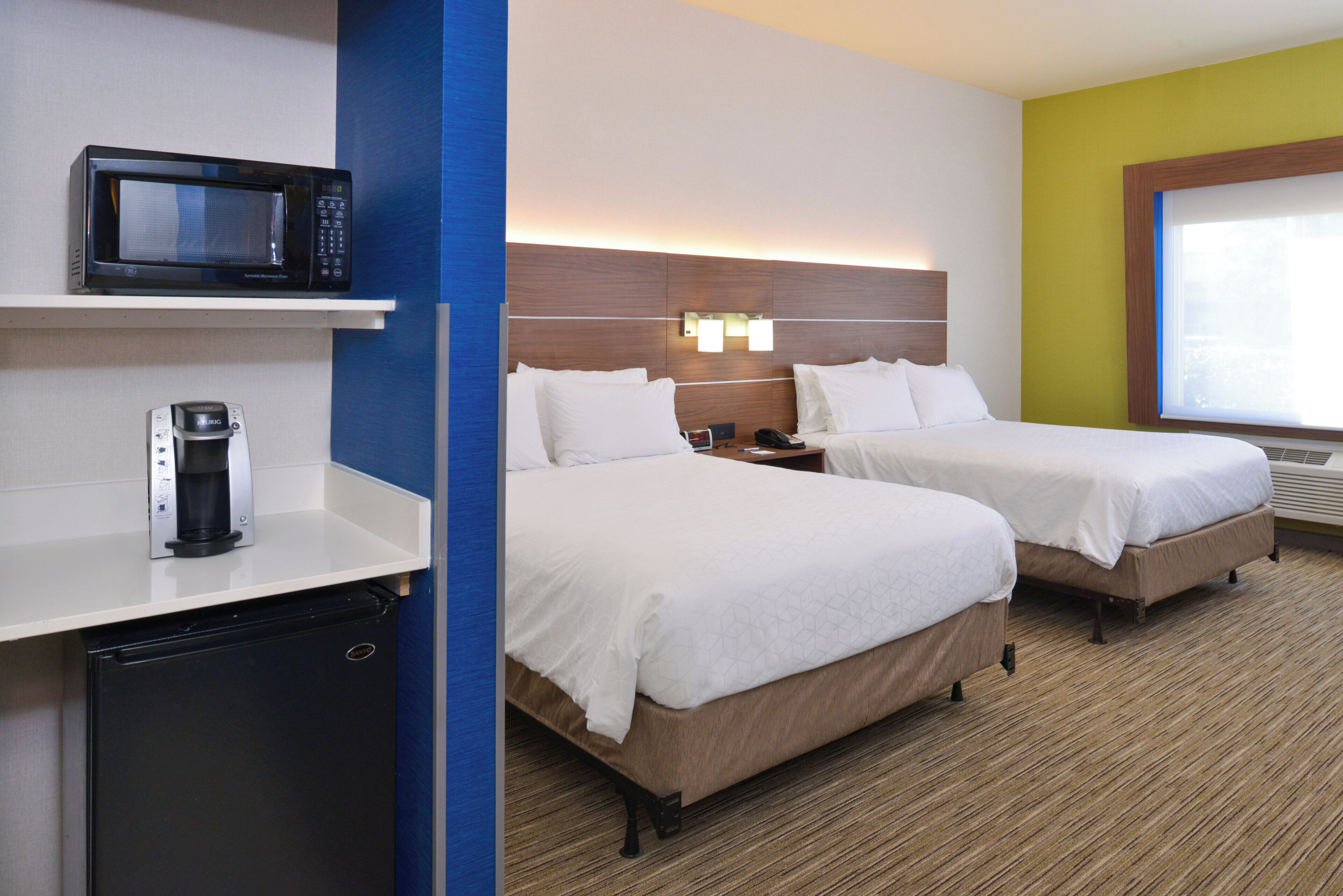 Een hotelkamer met twee bedden, een magnetron, een koffiezetapparaat en een kleine koelkast.