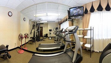 Un gimnasio con equipamiento de ejercicio, una cinta de correr y un televisor en la pared.