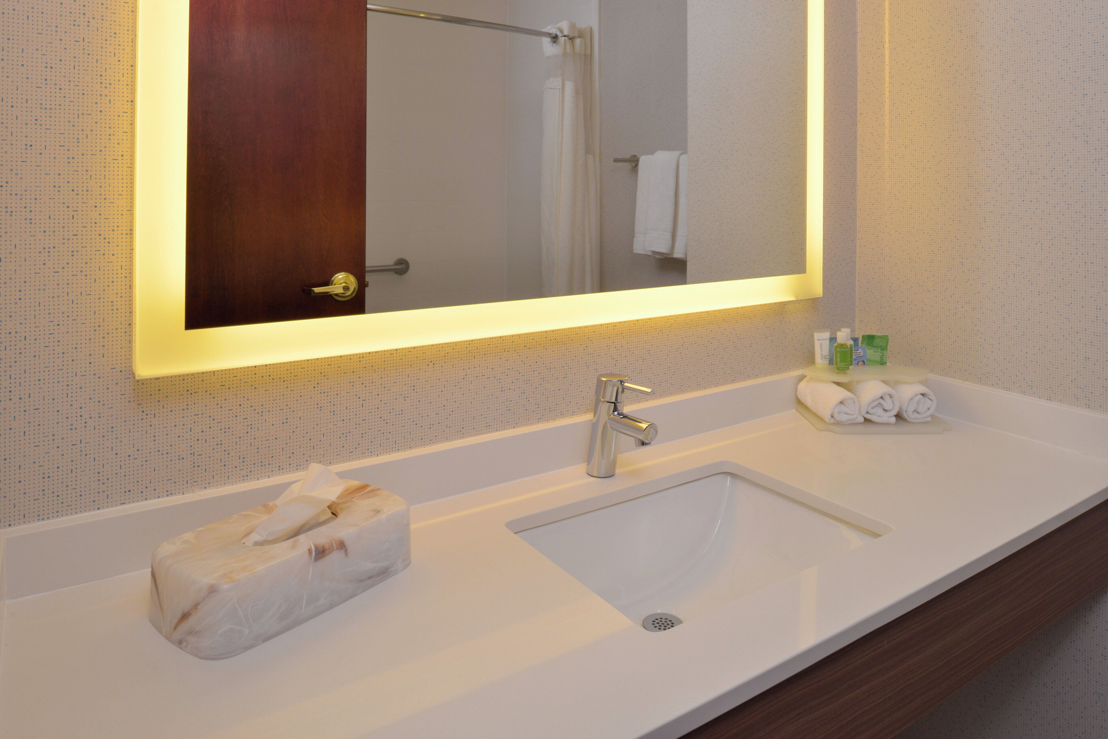 A bathroom with a white sink, a mirror with a lighted frame, and toiletries on the counter.