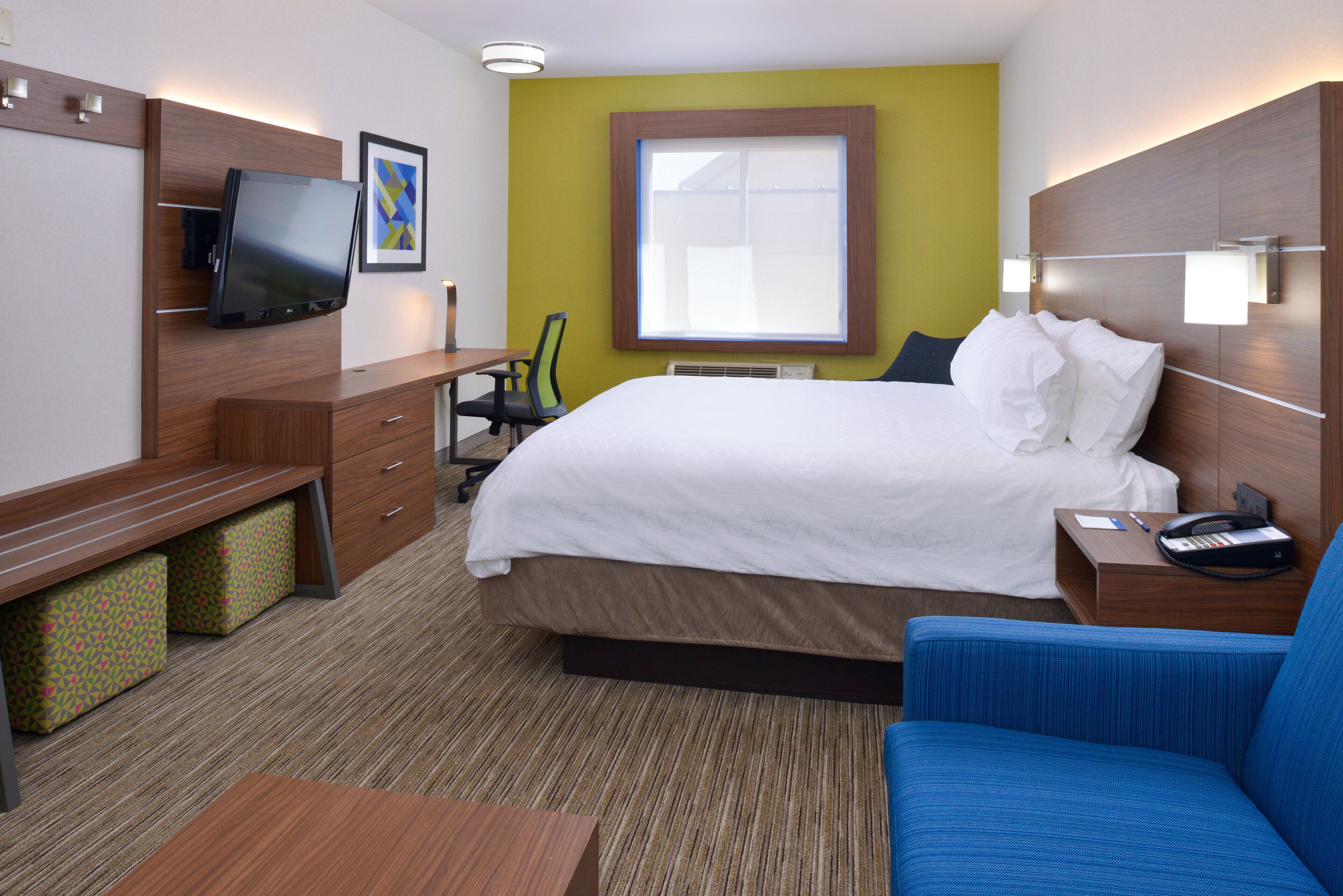 Una habitación de hotel con cama, escritorio, silla, televisor y ventana.
