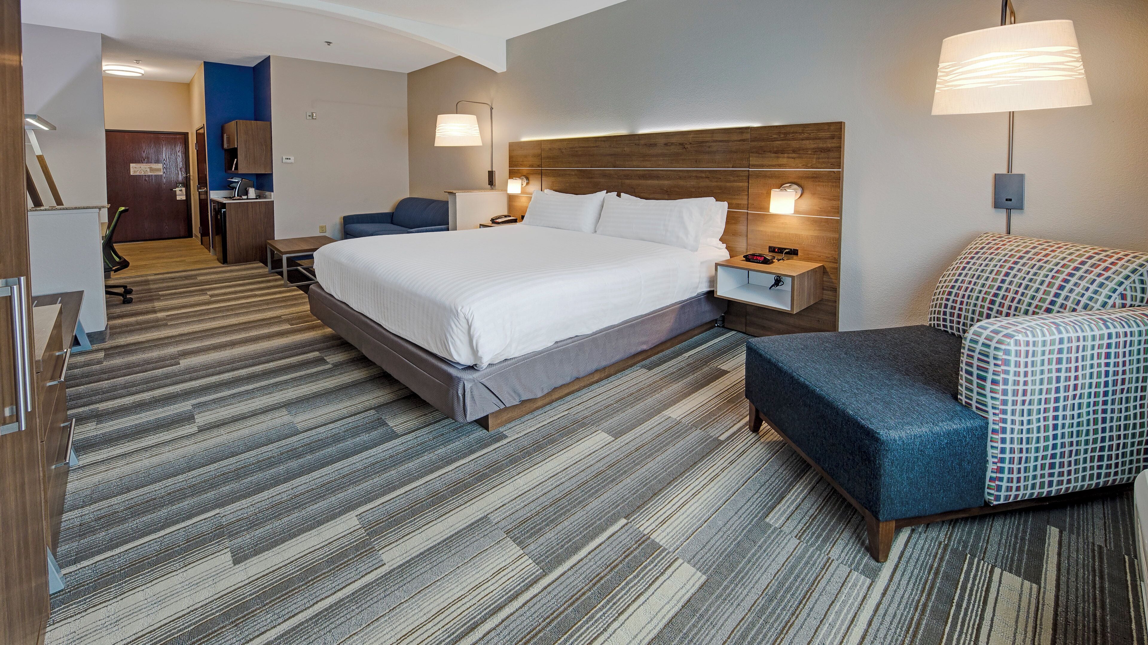 A hotel room with a large bed, a desk, a chair, and a patterned rug.