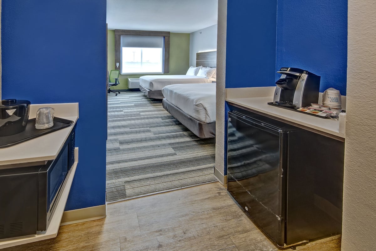 A hotel room with a kitchenette, a bed, a desk, and a window.